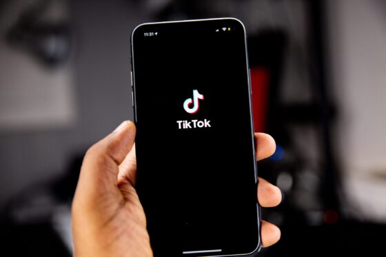 Person holding phone with TikTok logo against a black background