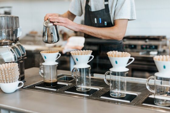 male barista preparing pour-over coffee, 4 white coffee cups waiting on the counter for hot water
