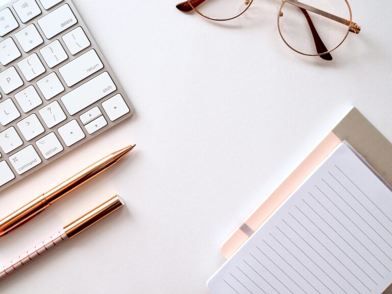 Gold pen next to mac keyboard on white table